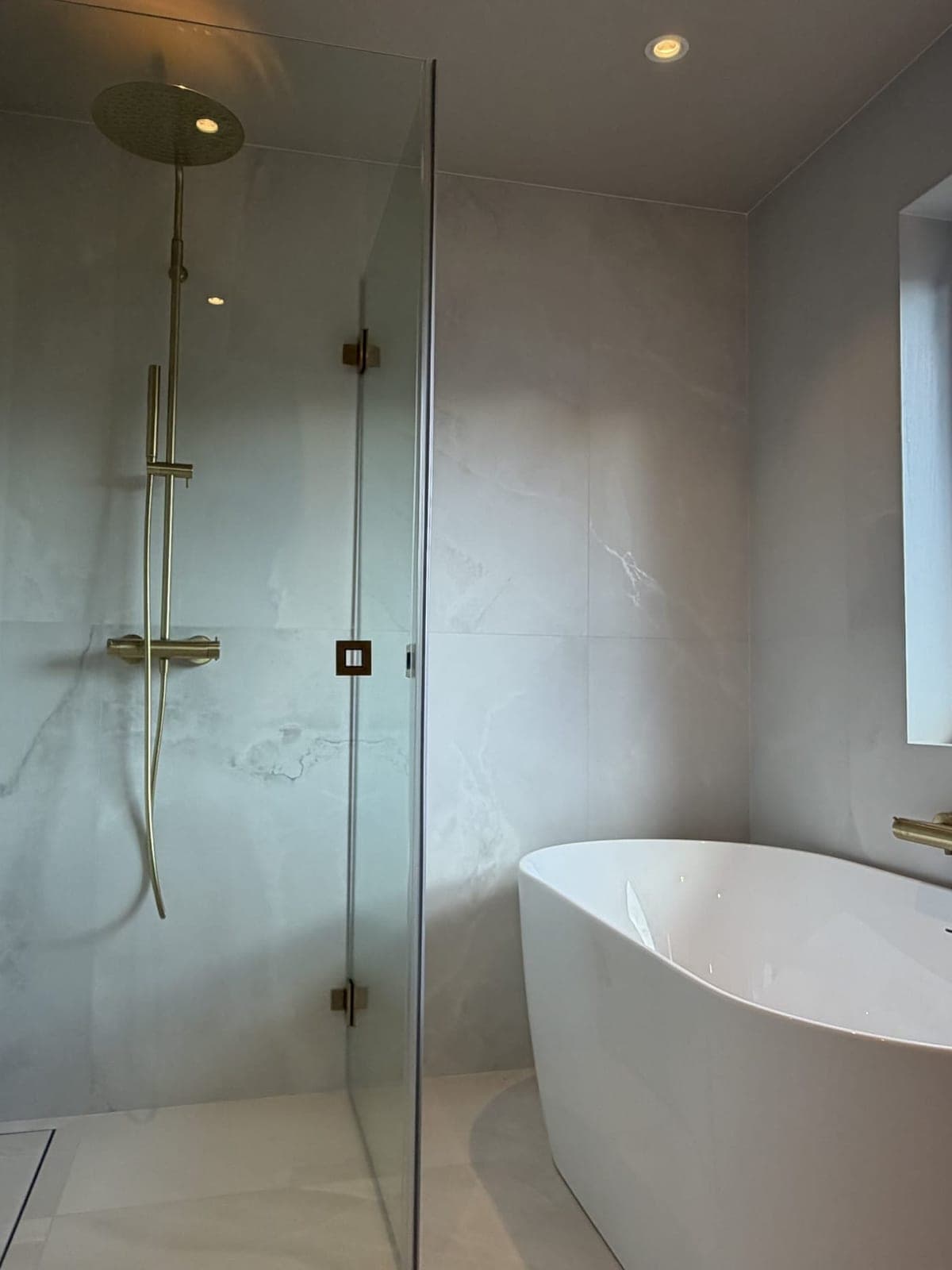 Walk-in-dusj bak glassvegg med armatur i messing og frittstående badekar på badet på Austflata i Trondheim